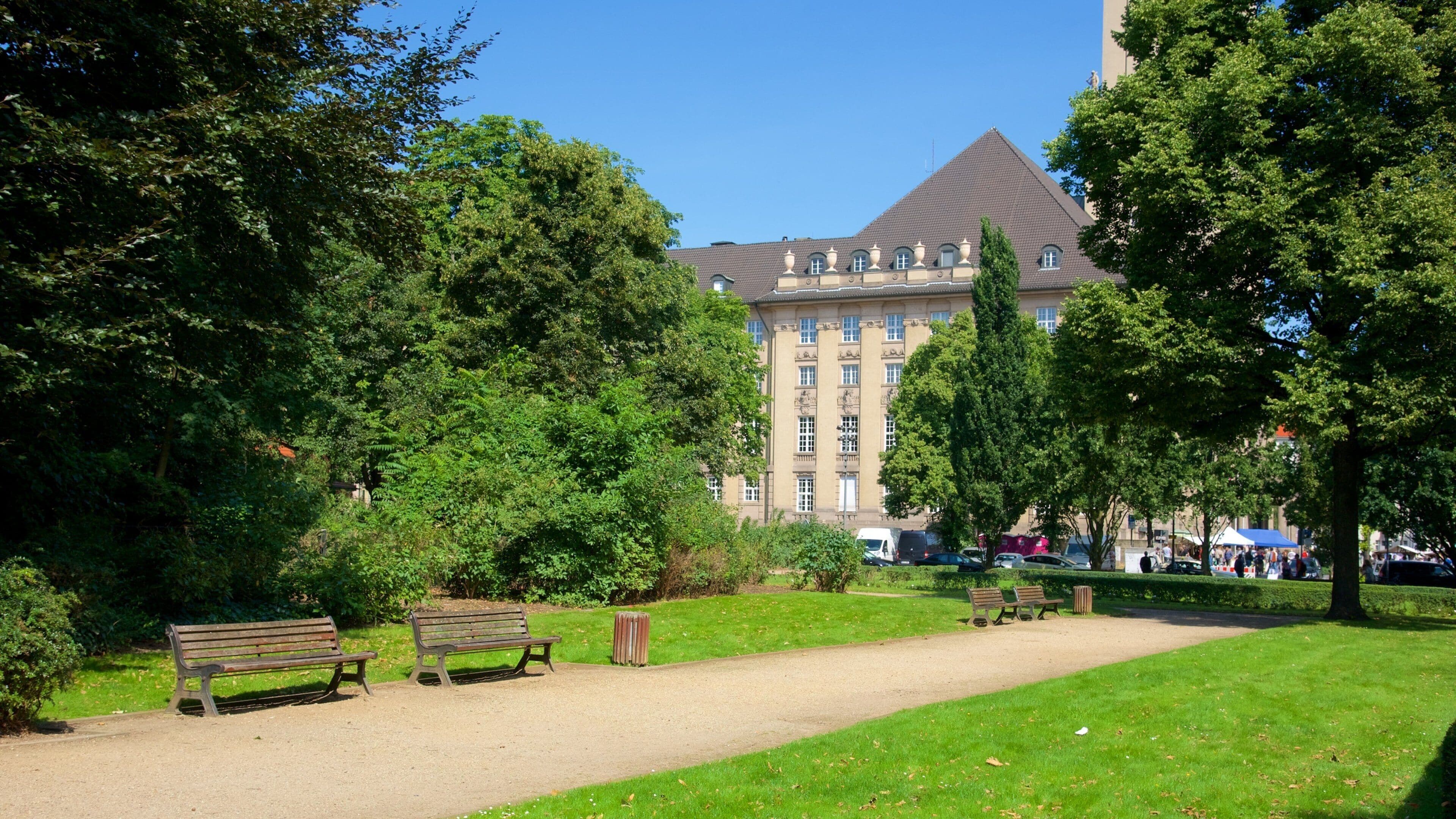 Ein Park mit Bänken, Bäumen und einem großen Gebäude im Hintergrund.