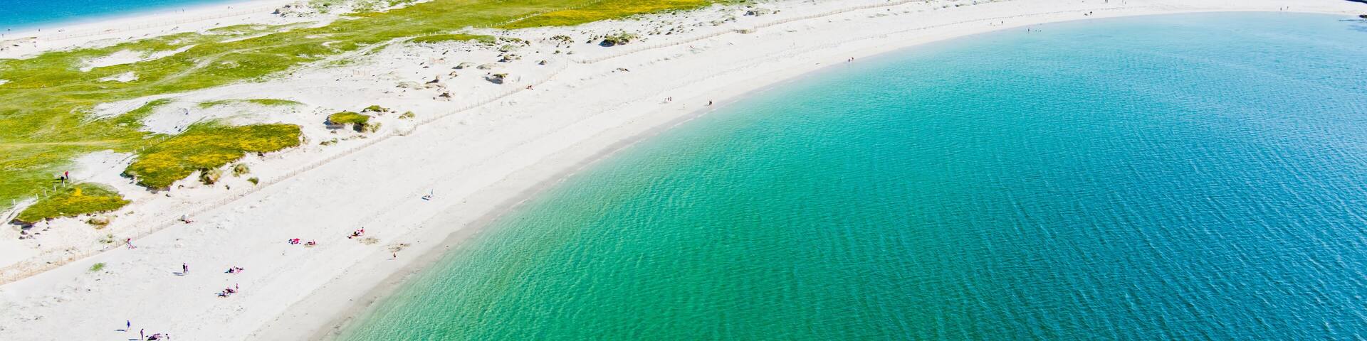A coastal landscape with a white sandy beach, clear turquoise waters, and a distant island.
