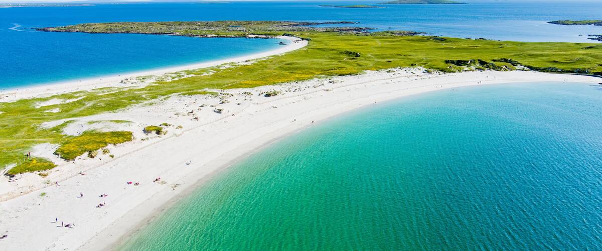 A coastal landscape with a white sandy beach, clear turquoise waters, and a distant island.