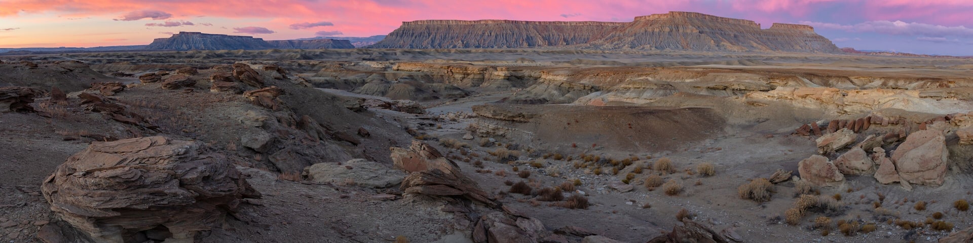 A vast desert landscape with rocky terrain and a prominent cliff formation under a pink and purple sky.