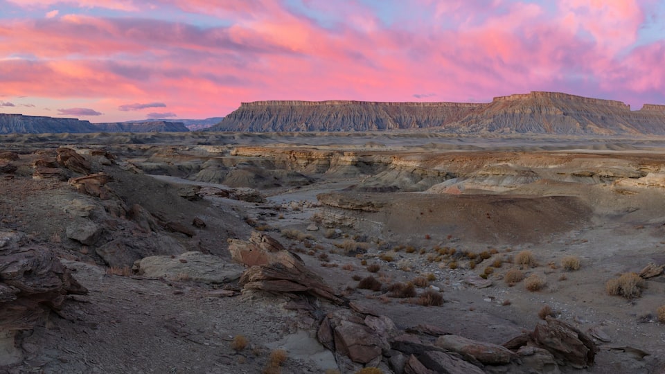 A vast desert landscape with rocky terrain and a prominent cliff formation under a pink and purple sky.