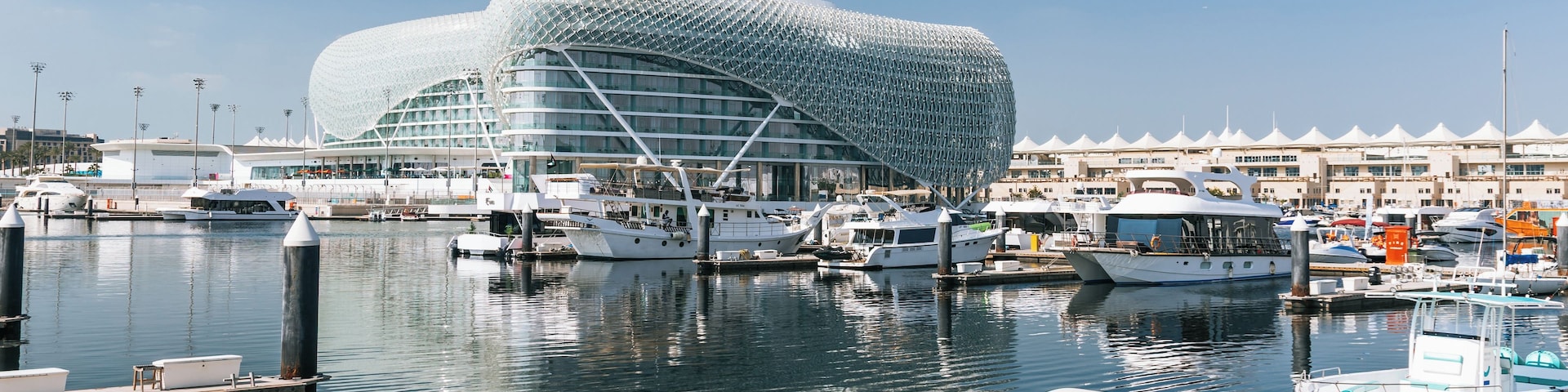 Un puerto deportivo con yates, un edificio moderno distintivo y un cielo azul despejado.