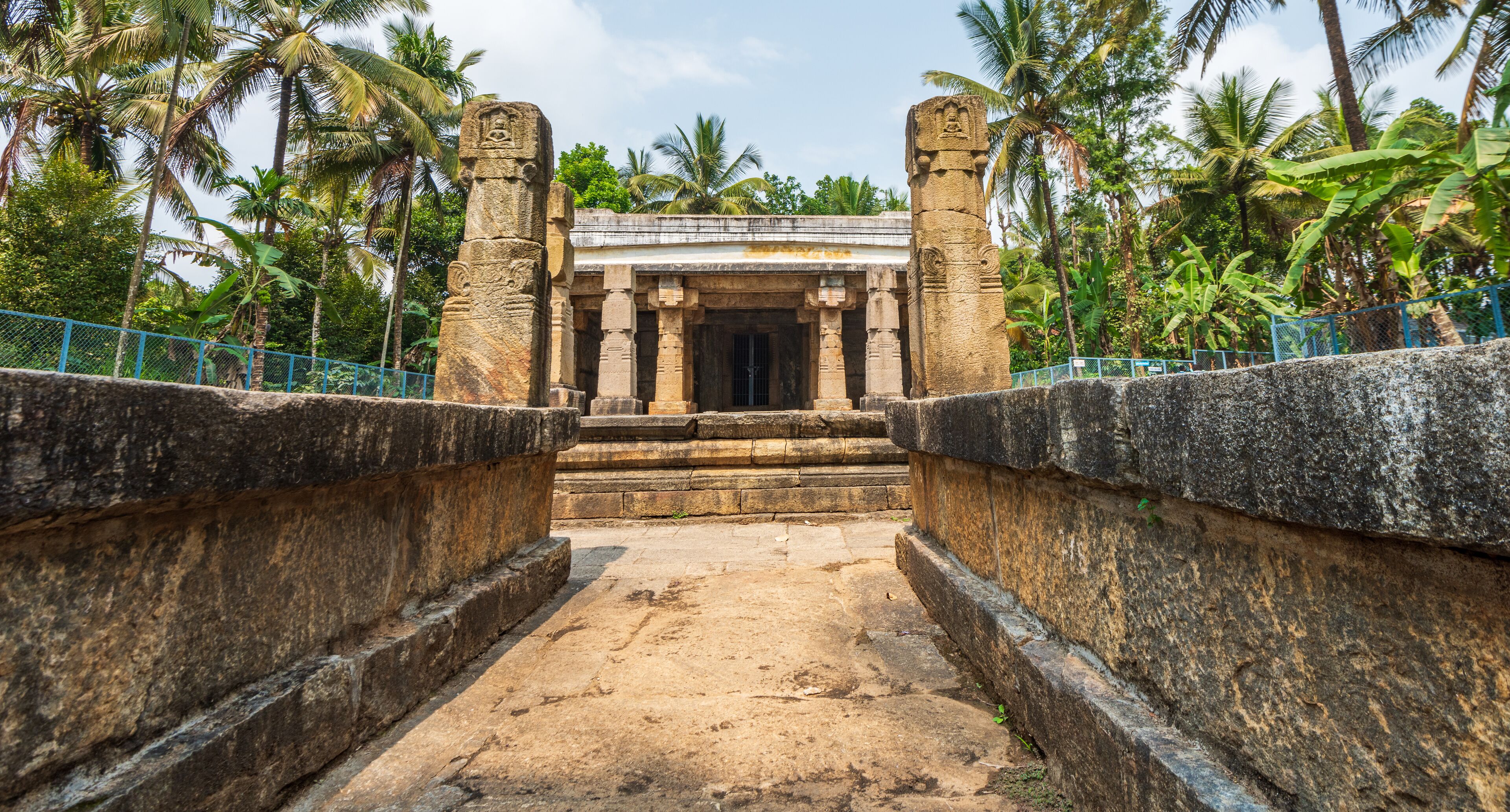 A stone temple entrance with steps leading up to it, surrounded by palm trees.