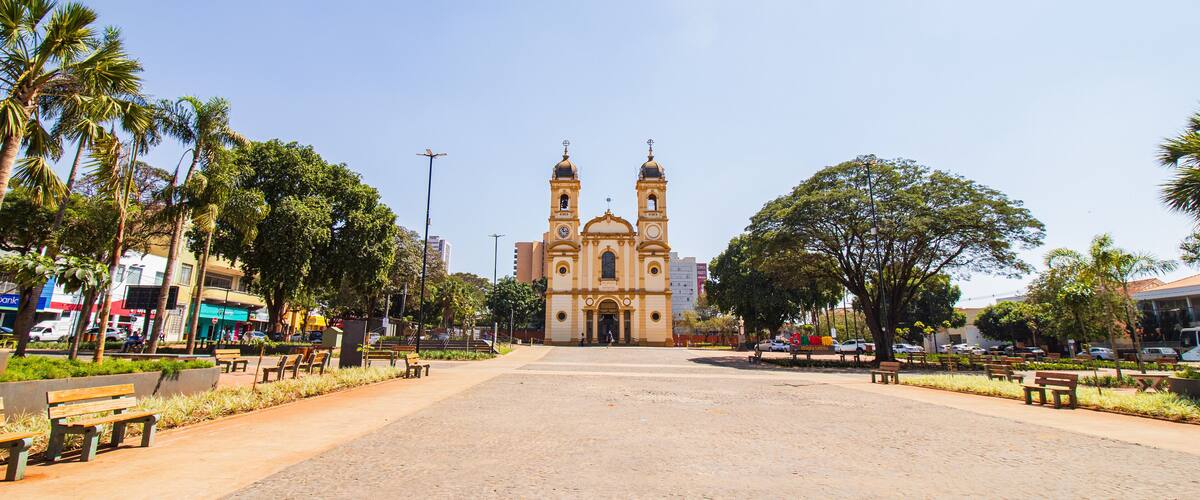 A plaza with a historic church, palm trees, benches, and a clear blue sky.