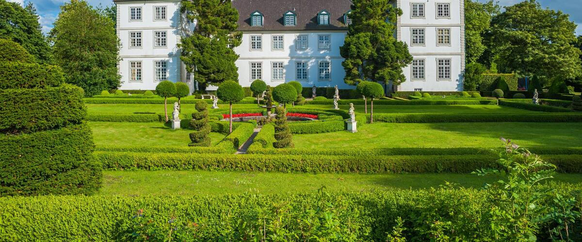 A large white building with a green roof, surrounded by well-manicured gardens and trees.