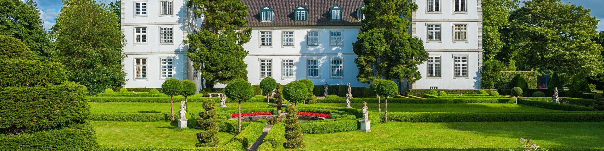A large white building with a green roof, surrounded by well-manicured gardens and trees.