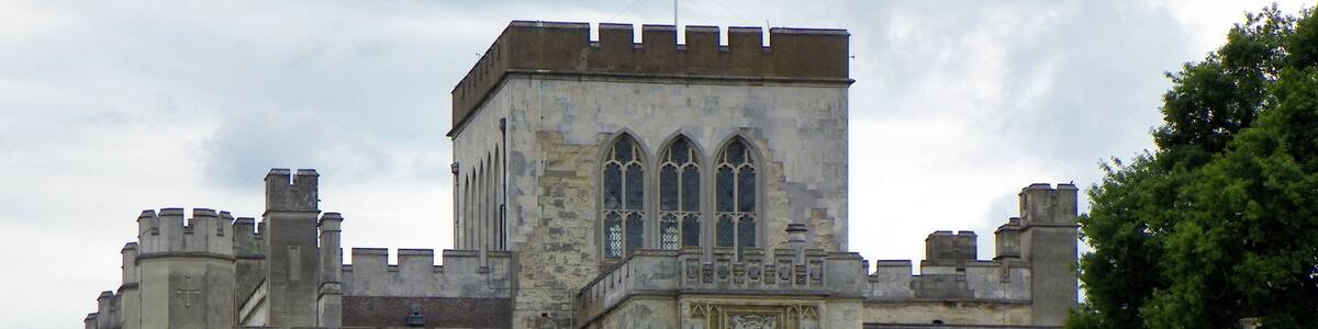 Ein historisches Steinhaus mit einem zentralen Turm, Rundbogenfenstern und einer Flagge.