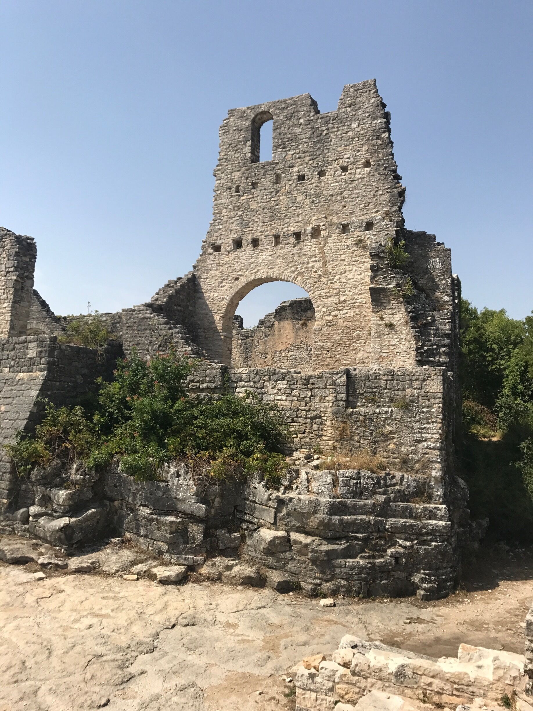A large stone tower with an arched entrance, surrounded by ruins and vegetation.