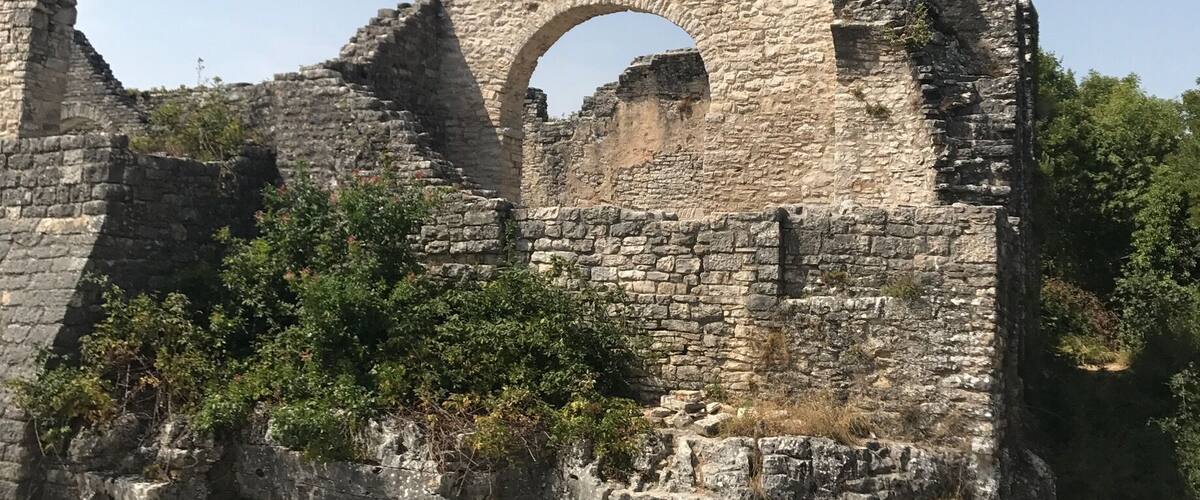 A large stone tower with an arched entrance, surrounded by ruins and vegetation.