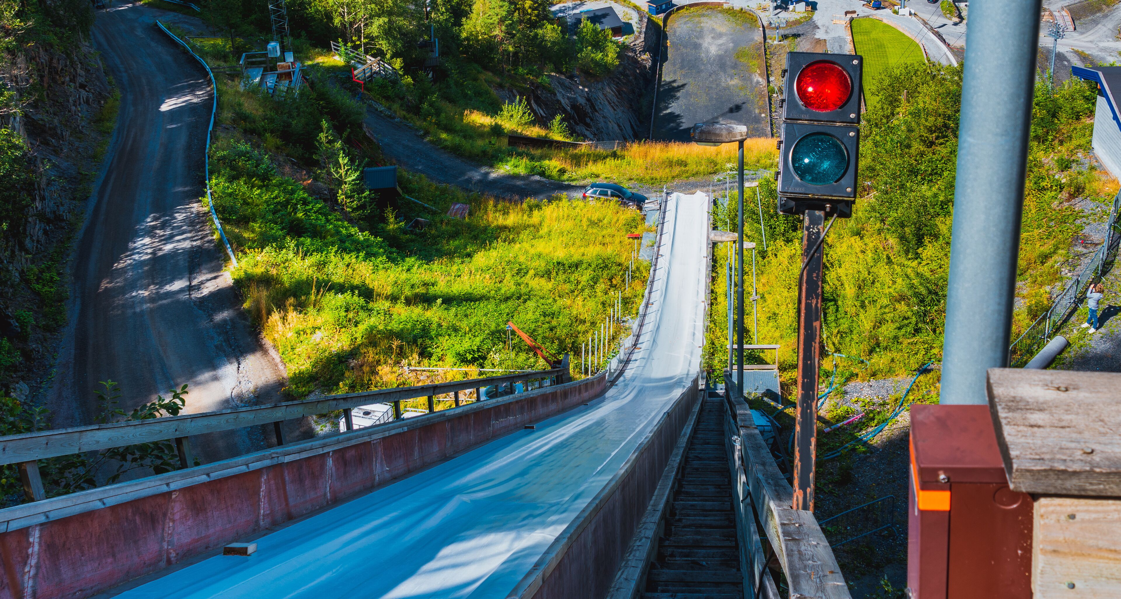 A steep road with a guardrail, a traffic light, and a bridge over a river.