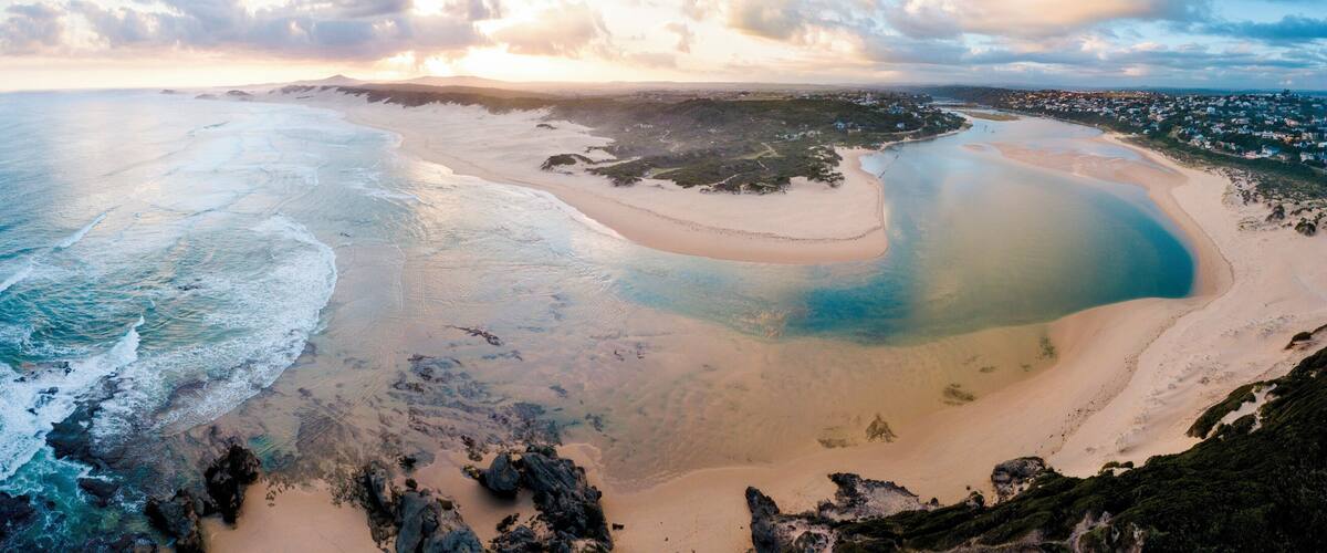 A coastal landscape with a large bay, sandy beaches, rocky outcrops, and a distant town.