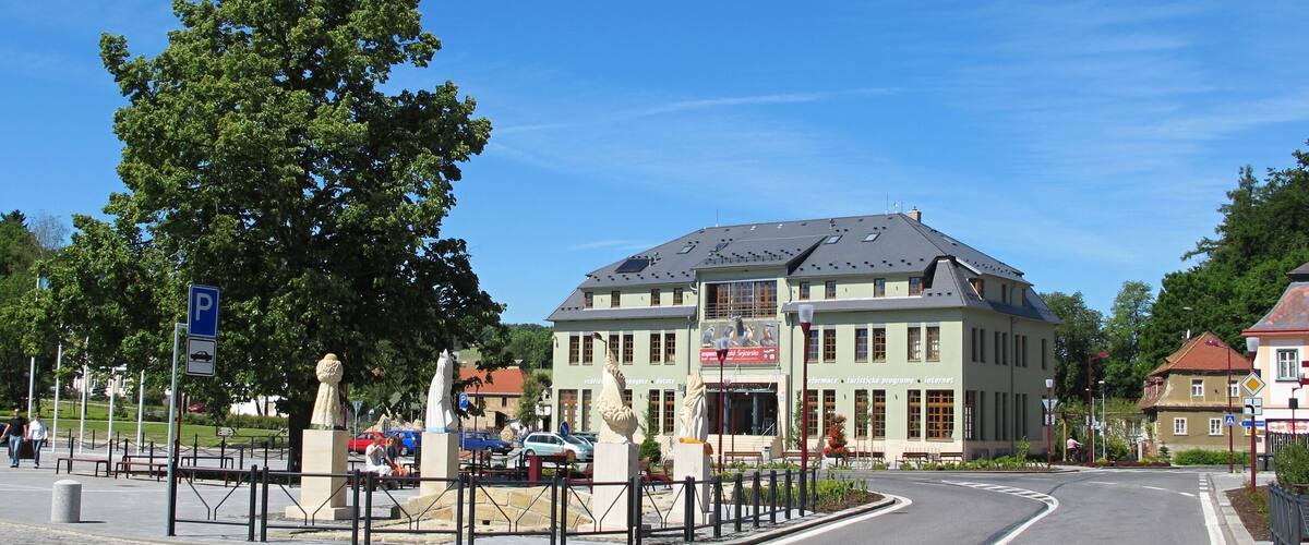 A building with a green roof and a signboard, surrounded by trees and a clear blue sky.
