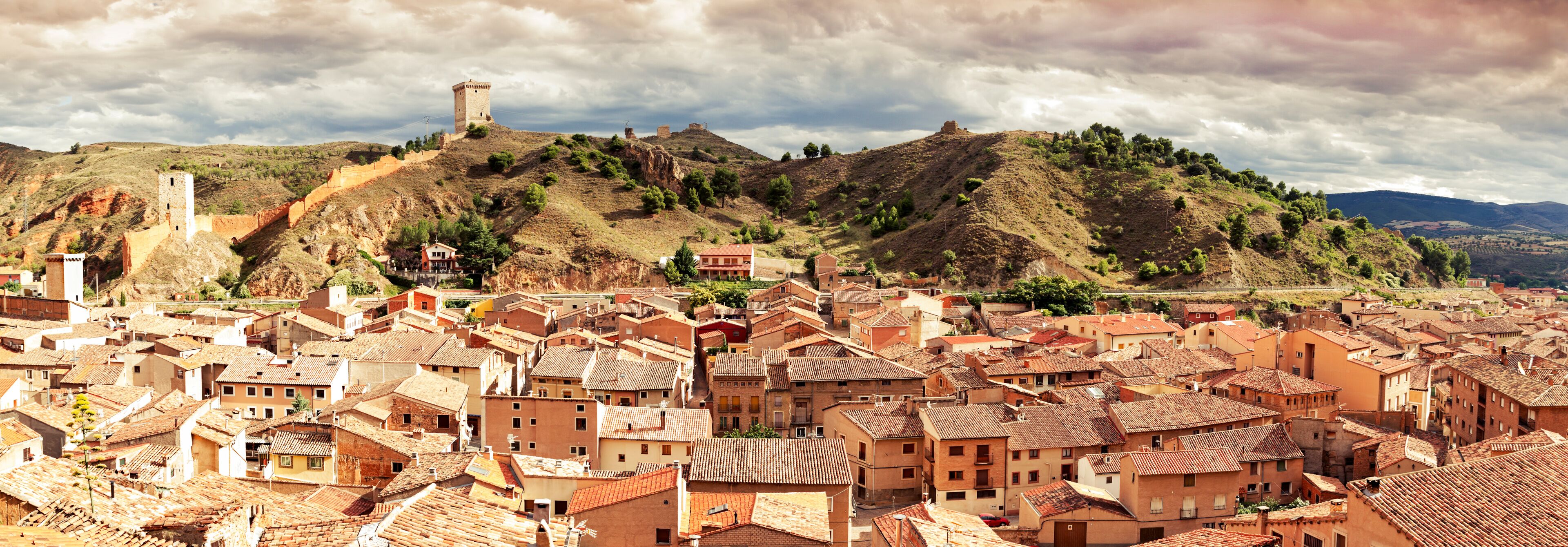 A town with terracotta-roofed buildings, a hilltop tower, and a valley.