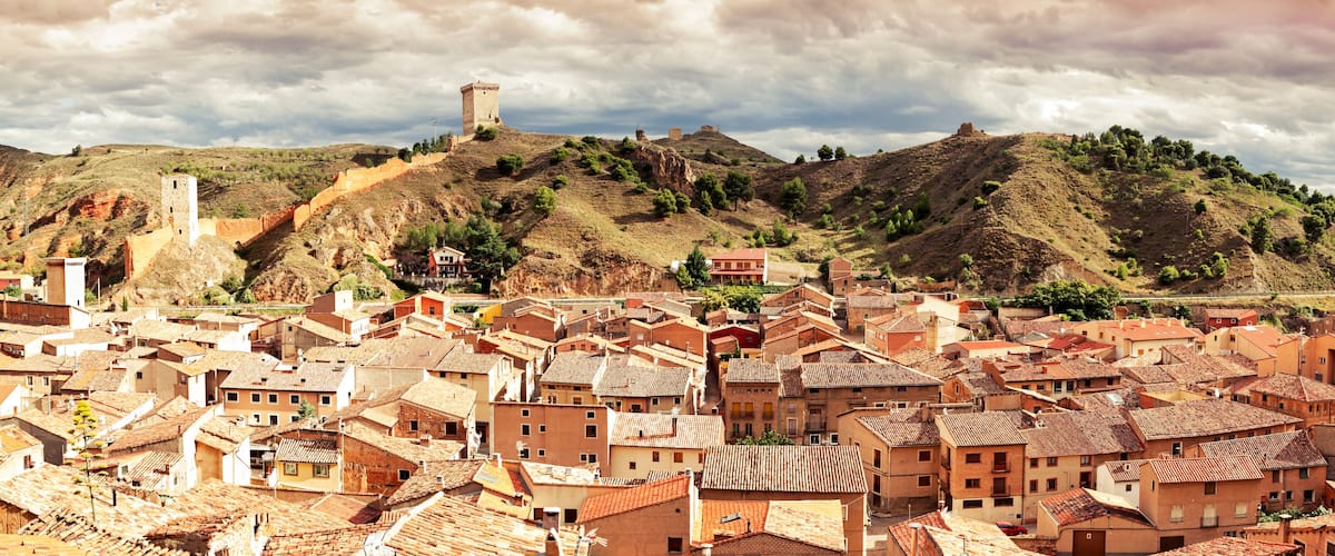 A town with terracotta-roofed buildings, a hilltop tower, and a valley.