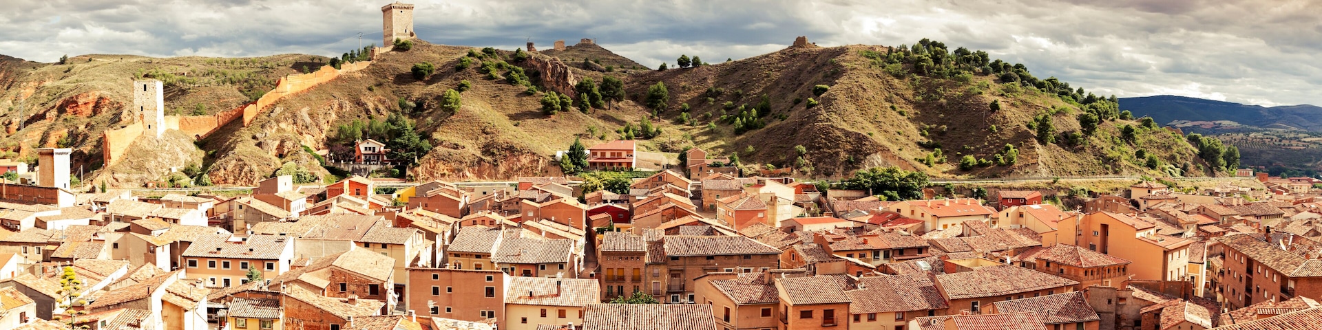 A town with terracotta-roofed buildings, a hilltop tower, and a valley.