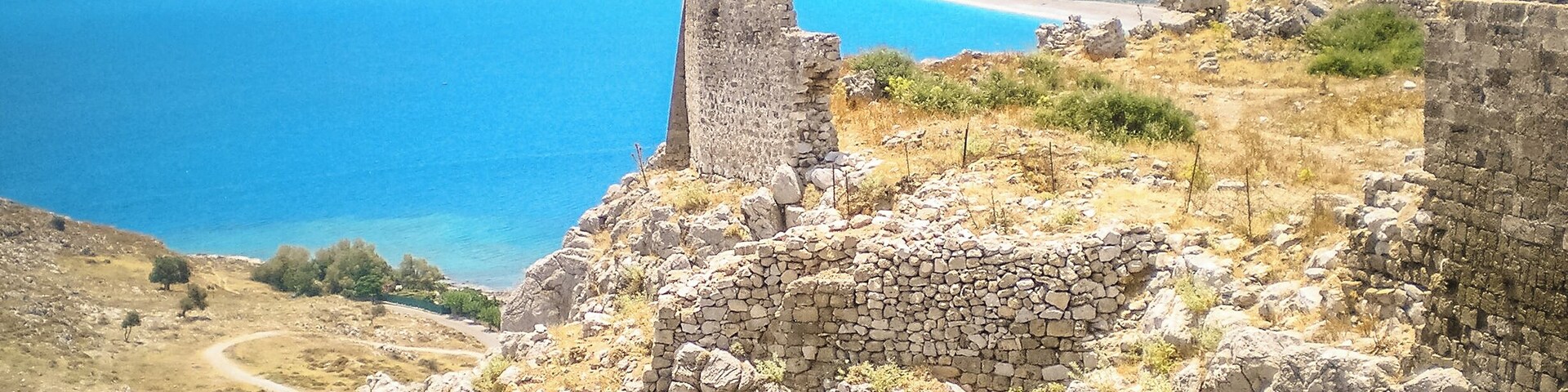 A coastal landscape with ancient ruins and a clear blue sea.