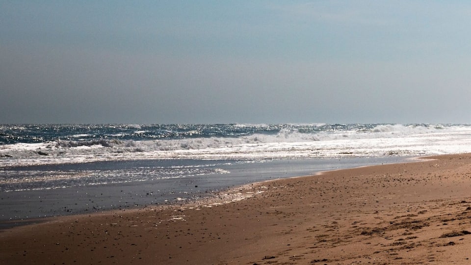 A sandy beach with waves crashing onto the shore and a few people walking along the beach.