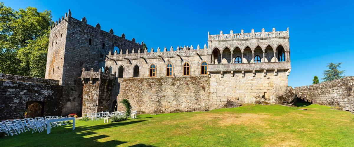 A historic stone castle with a tall tower, arched windows, and a well-maintained lawn.