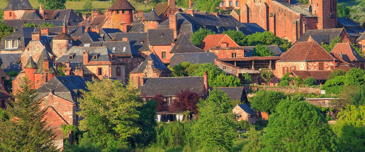 A historic town with red brick buildings, a prominent church with a tall tower, and lush green hills in the background.