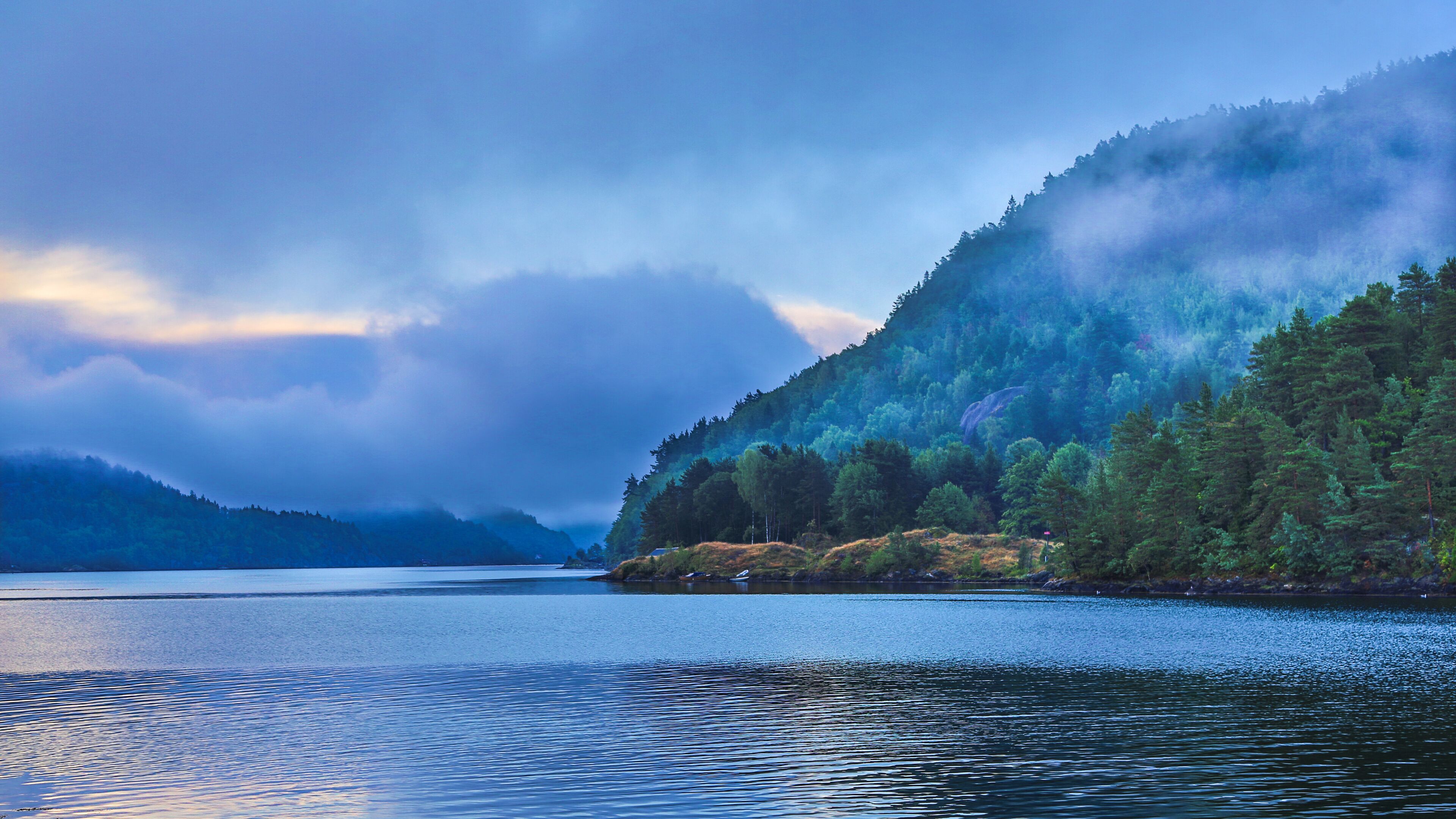 A calm lake surrounded by dense forests and mist-covered mountains.