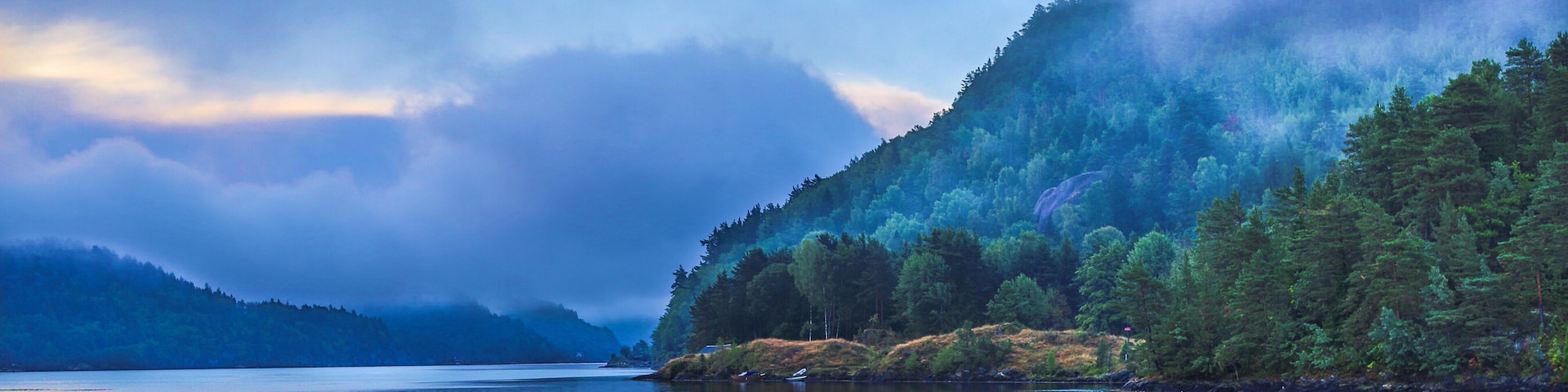 A calm lake surrounded by dense forests and mist-covered mountains.