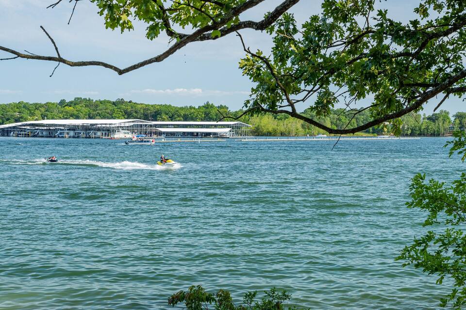 A lake with a boat speeding across the water, a docked boat, and a building with a white roof in the background.