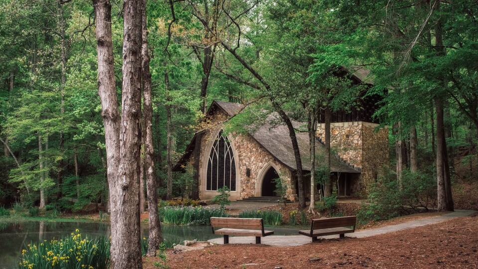 A stone chapel surrounded by trees and a pond.