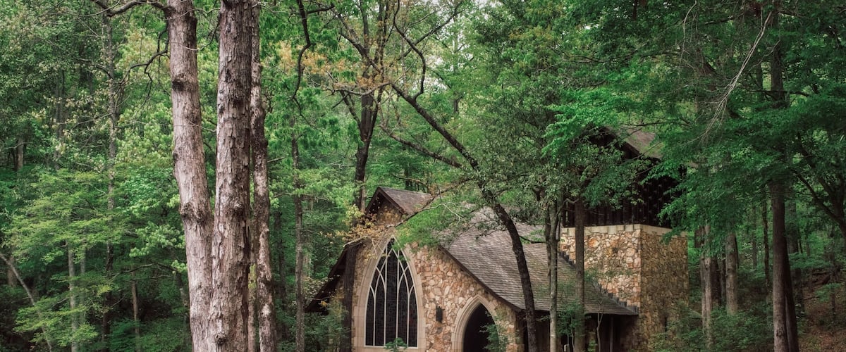 A stone chapel surrounded by trees and a pond.