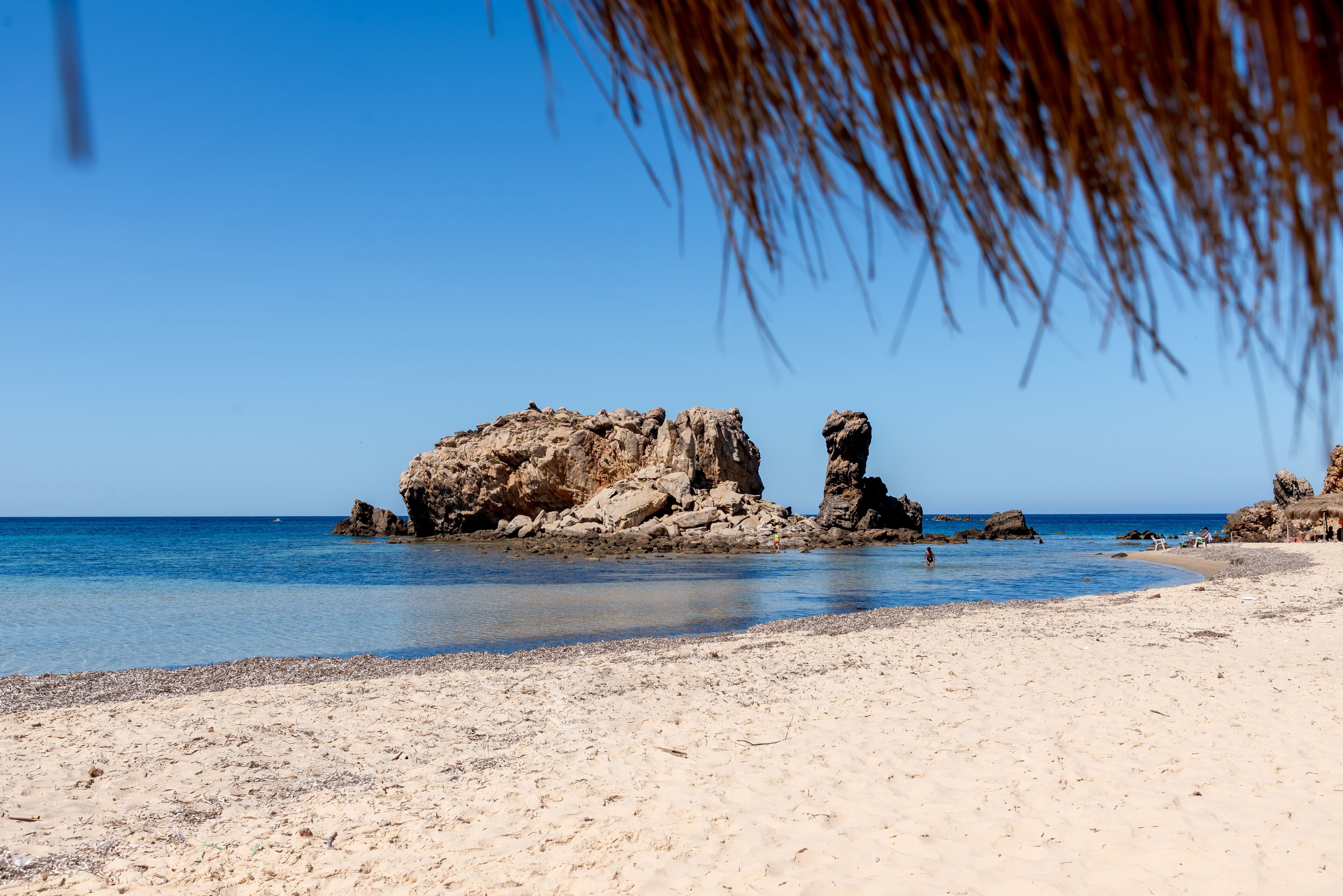 A sandy beach with clear blue water, rocky formations, and a clear sky.