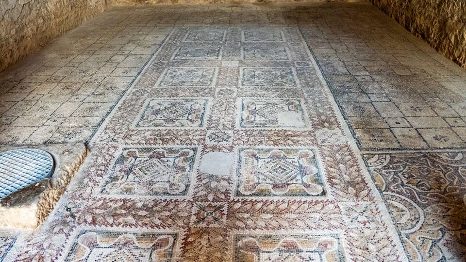 An ancient mosaic floor with geometric patterns and a central square.