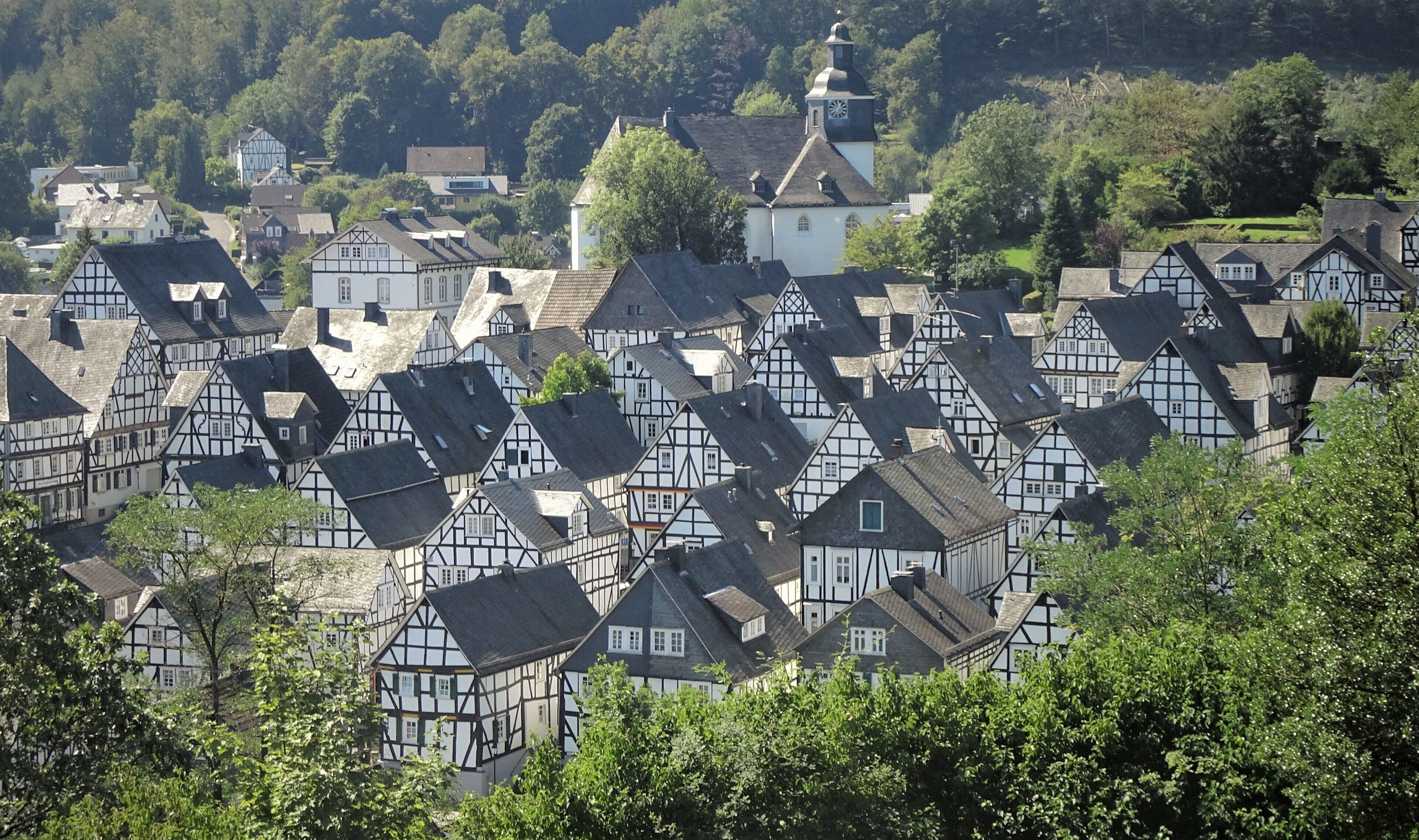 A village with traditional half-timbered houses, surrounded by lush greenery and a prominent church steeple.