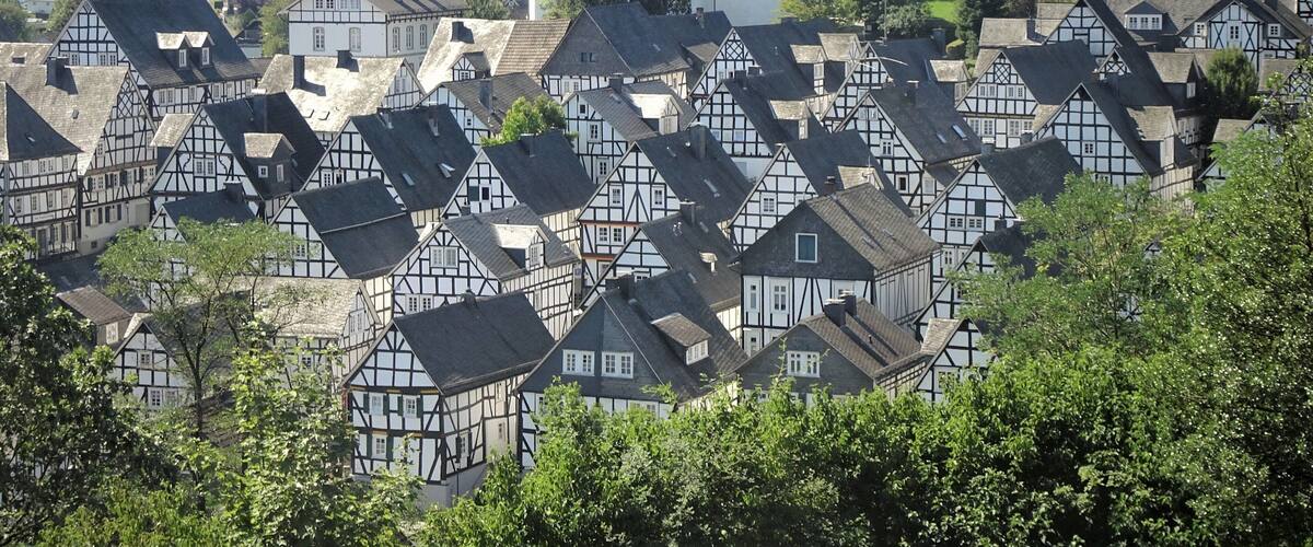 A village with traditional half-timbered houses, surrounded by lush greenery and a prominent church steeple.