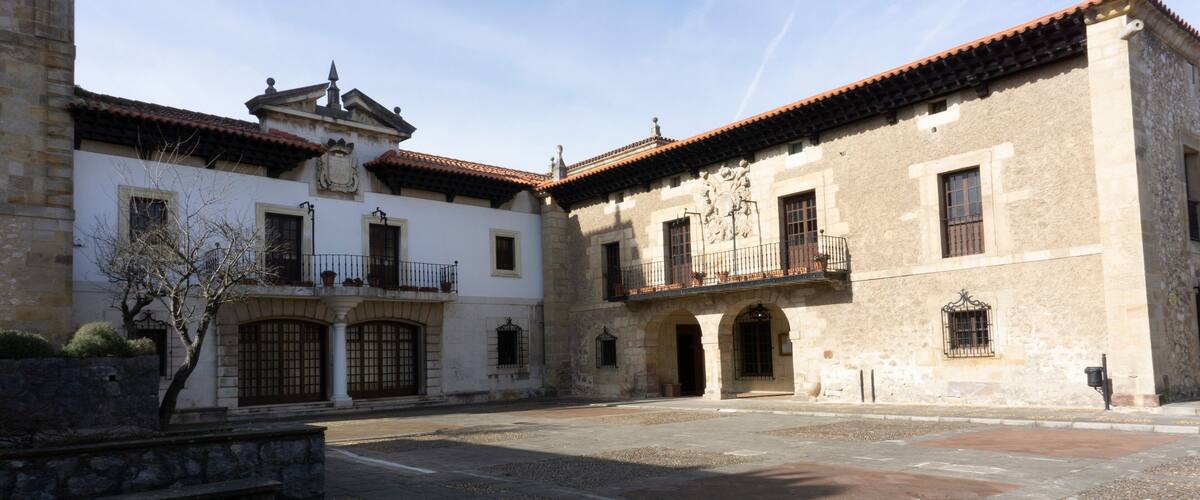 A courtyard with a fountain, a white building with a red-tiled roof, and a stone wall.