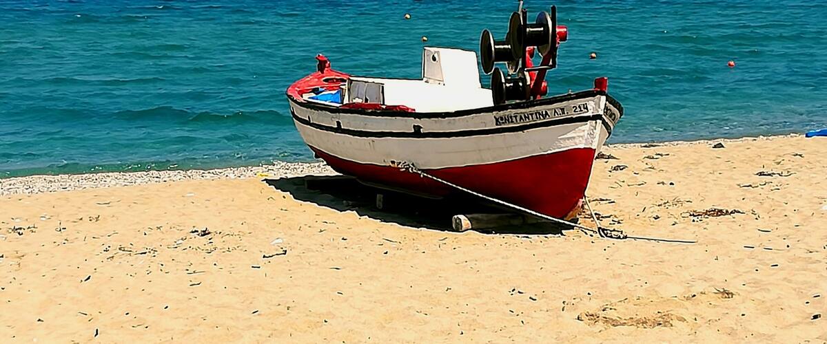 A red and white boat named "CHRISTINA A.M. 214" on a sandy beach with the ocean in the background.