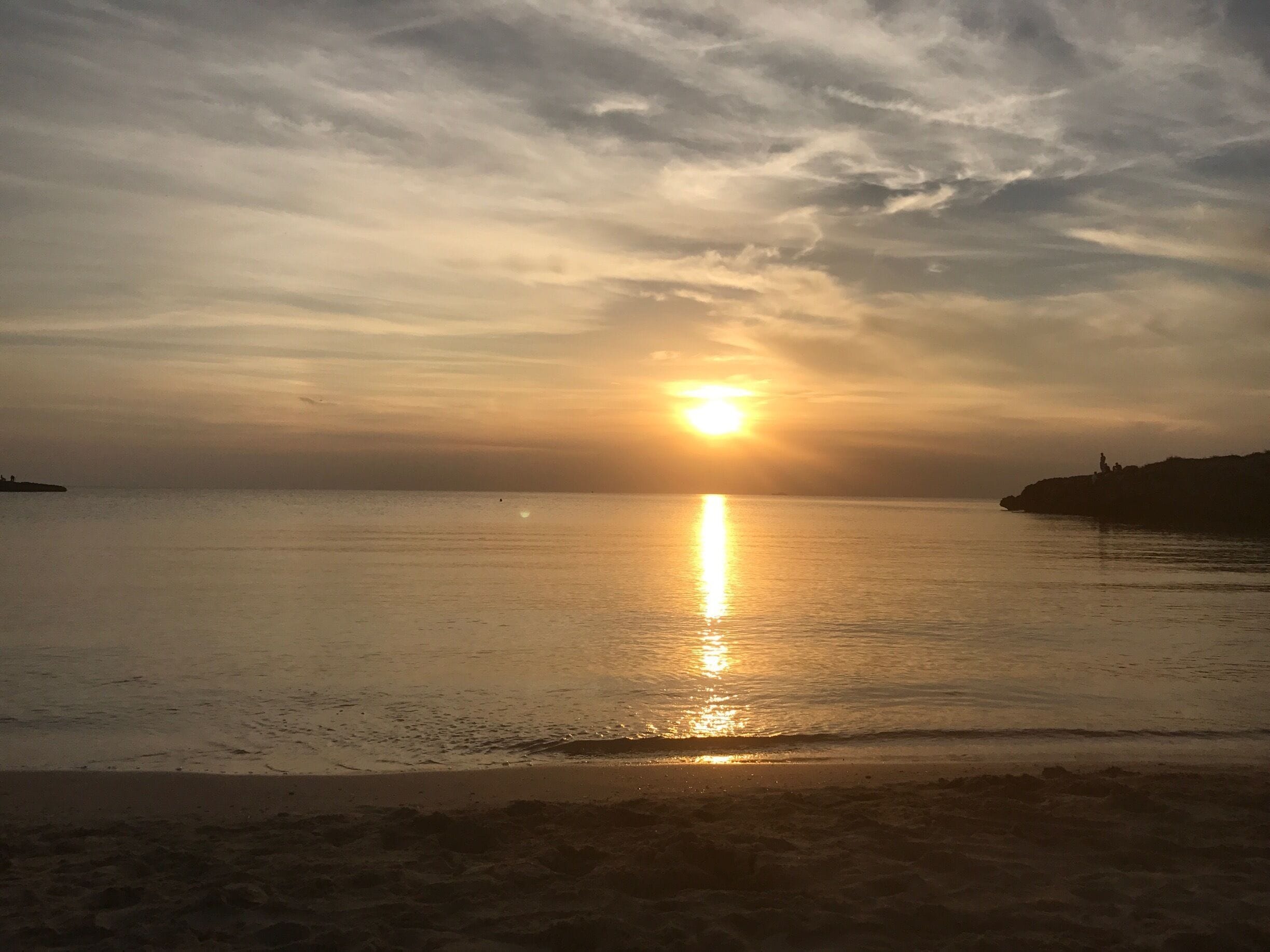A sunset over a calm sea with a silhouette of a rocky coastline.