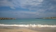 Une plage bordée d’une eau turquoise et limpide, avec de douces vagues et une côte rocheuse qui s’étend au loin.