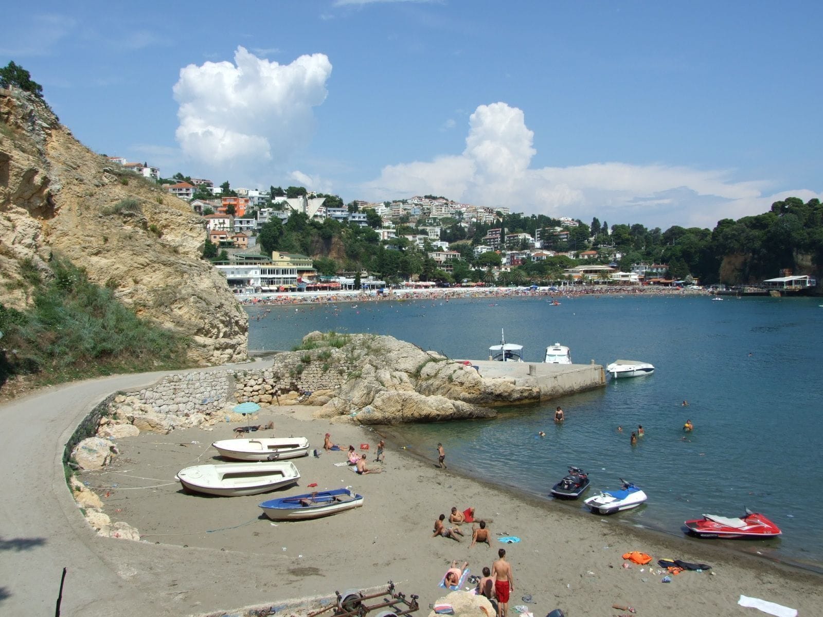 A beach with boats, people, and a town in the background.