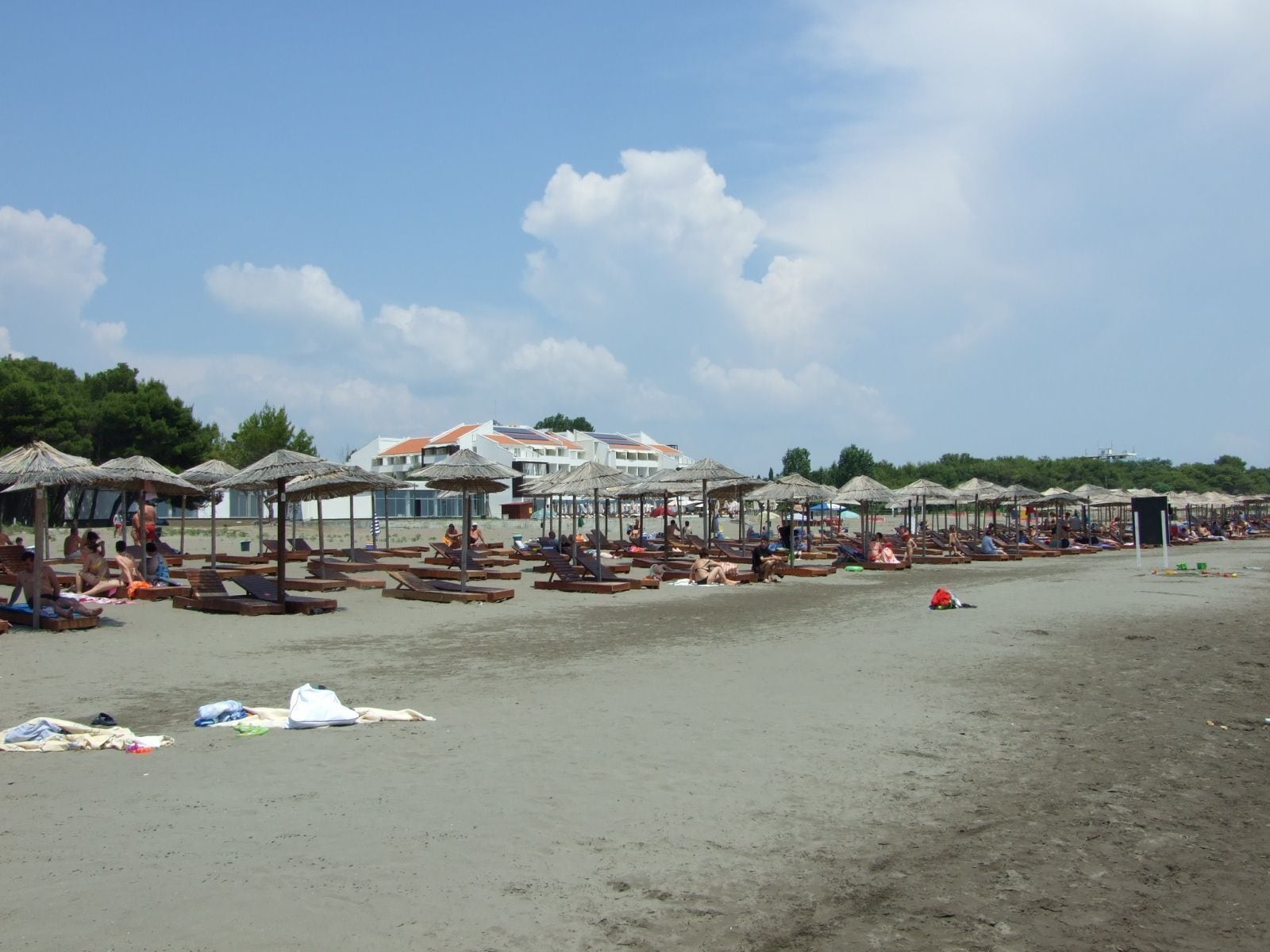 A beach with wooden sun loungers and thatched umbrellas under a clear sky.