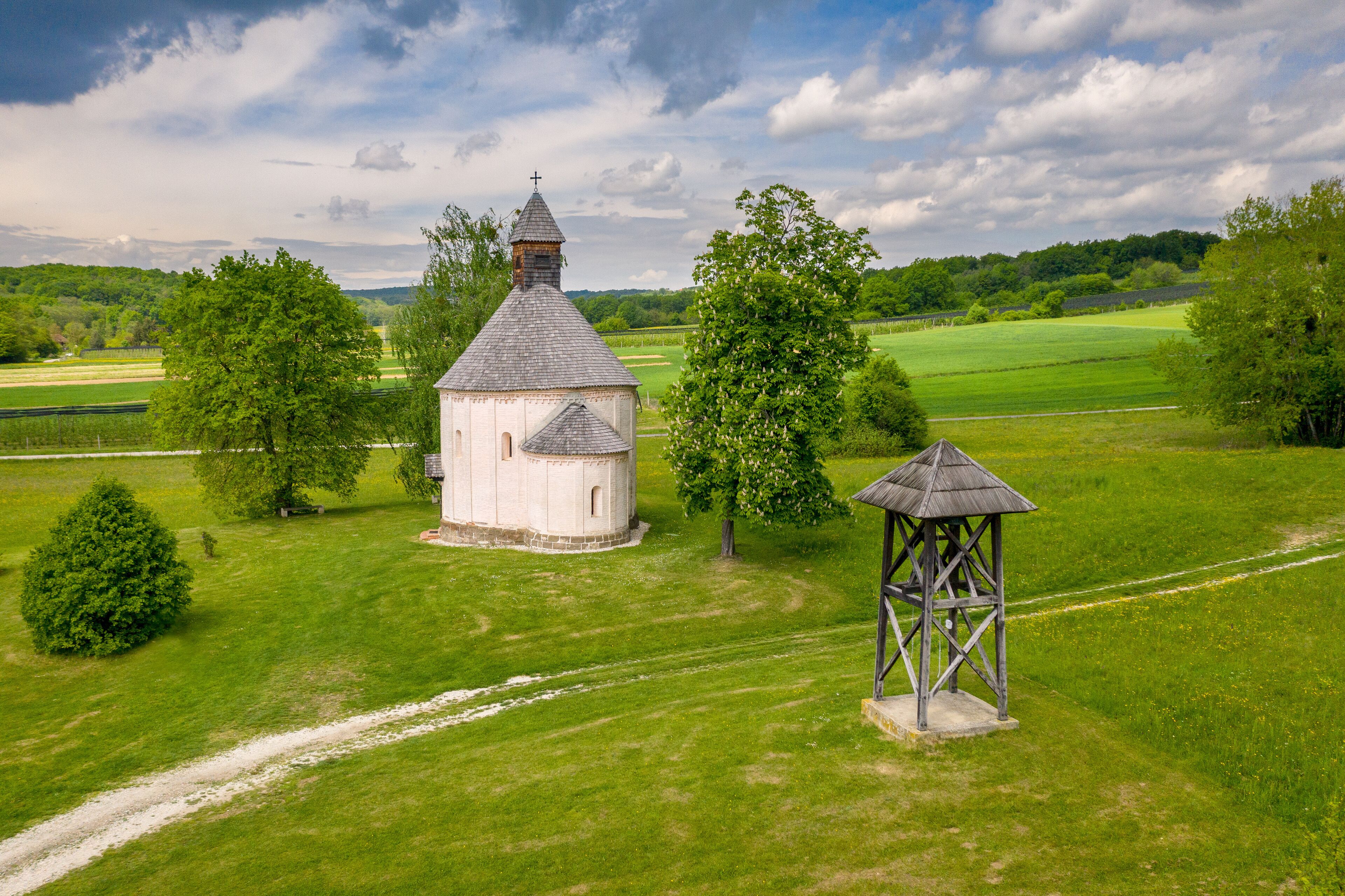A white church with a bell tower and a wooden gazebo in a lush green field.