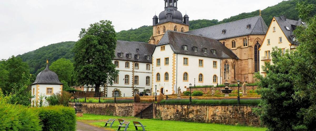 A historic building with a prominent tower, surrounded by lush greenery and a well-maintained garden.