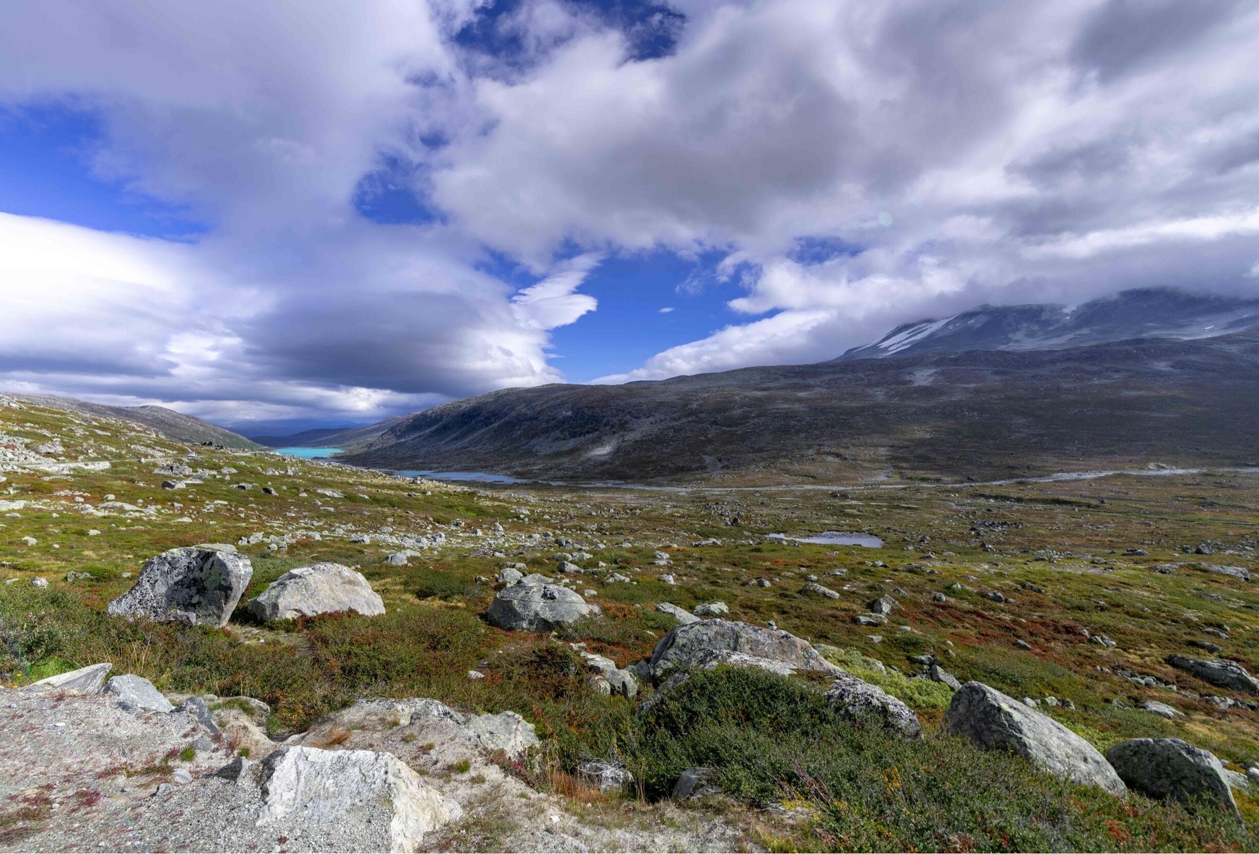 A mountainous landscape with rocky terrain and a distant lake under a partly cloudy sky.