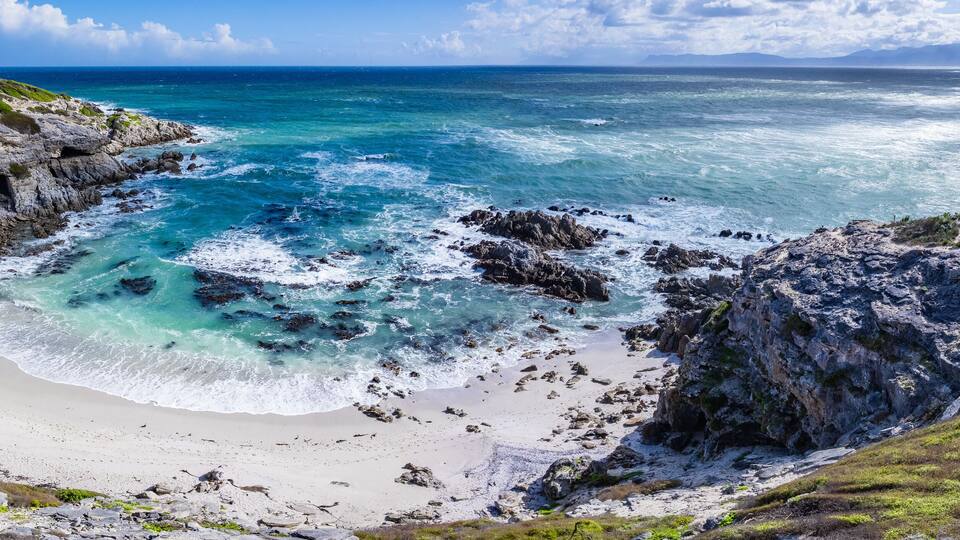 A coastal landscape with rocky cliffs, a sandy beach, and turquoise waters.