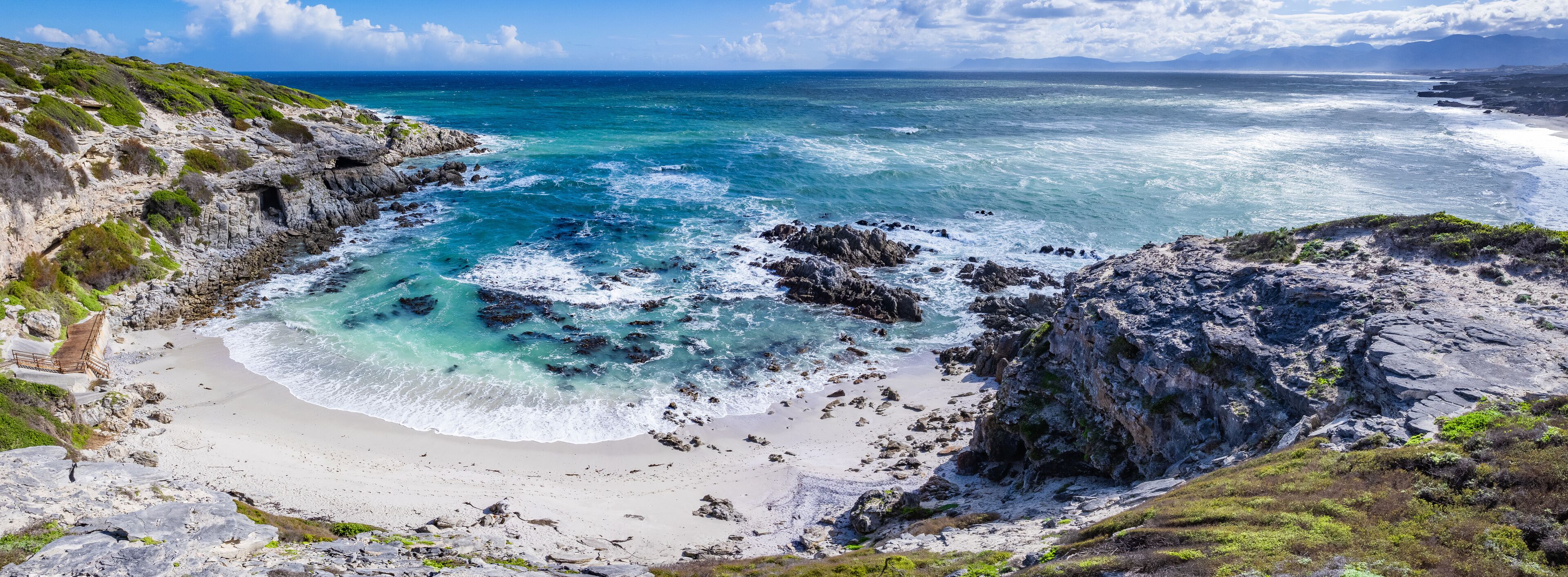 A coastal landscape with rocky cliffs, a sandy beach, and turquoise waters.