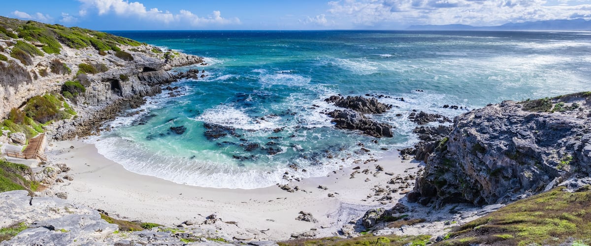 A coastal landscape with rocky cliffs, a sandy beach, and turquoise waters.