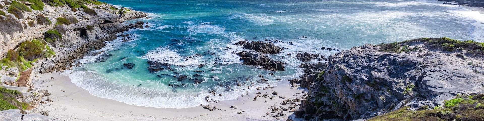 A coastal landscape with rocky cliffs, a sandy beach, and turquoise waters.