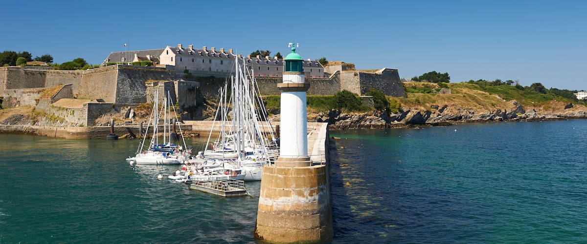 A lighthouse, boats, and a fortified building by the water.