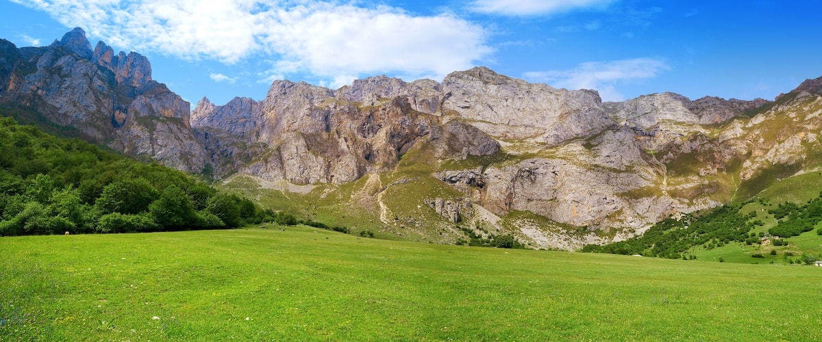 A mountainous landscape with a green meadow in the foreground and rocky cliffs in the background.