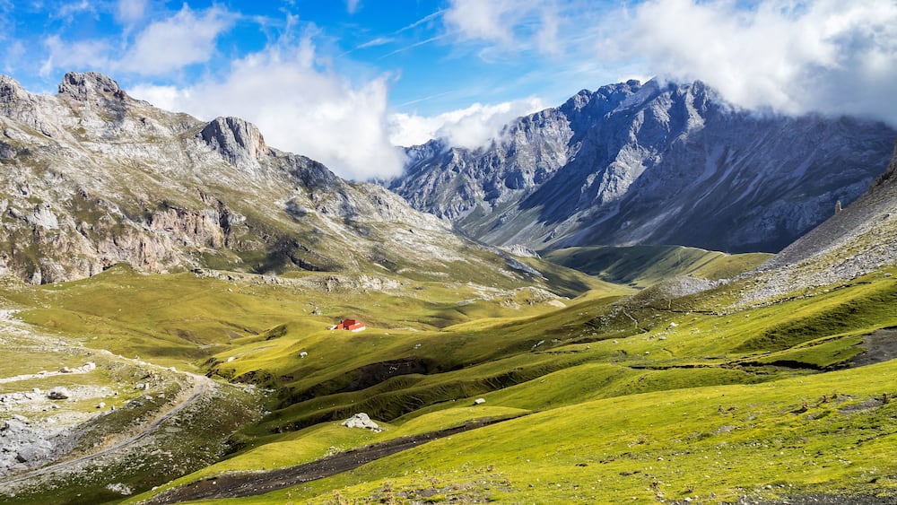 A mountainous landscape with a valley, a winding road, and a red building.