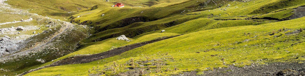 A mountainous landscape with a valley, a winding road, and a red building.