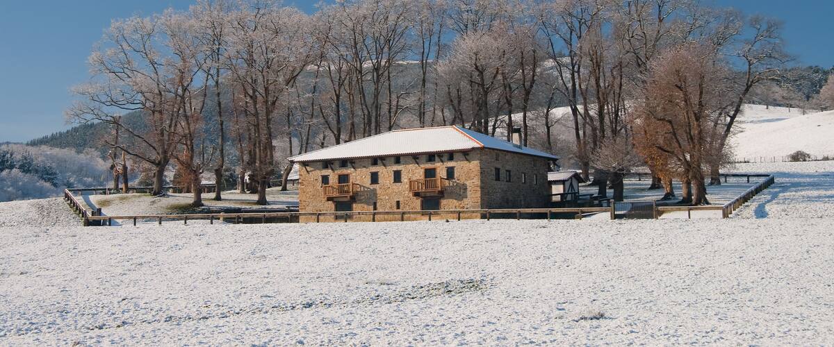 A snow-covered landscape with a stone building, bare trees, and a clear blue sky.
